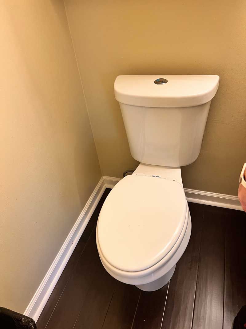 White toilet in a small bathroom with dark wood flooring and tan walls.