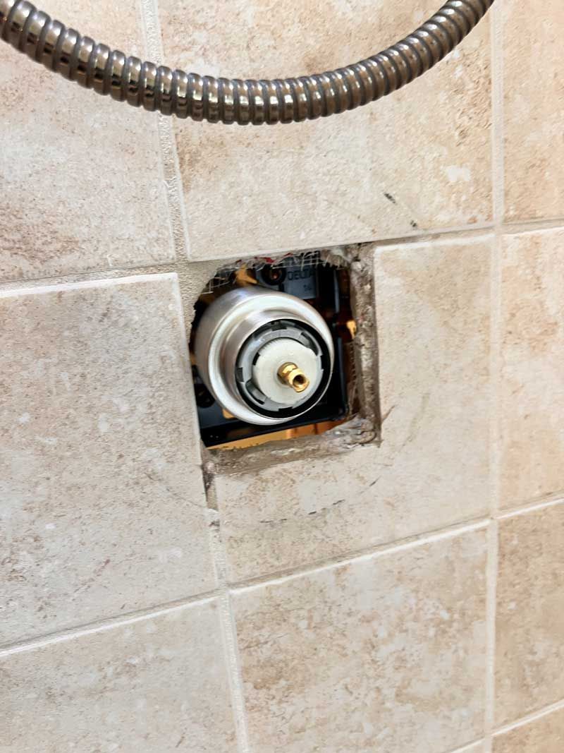 Shower valve assembly exposed in tiled wall, shower hose overhead.