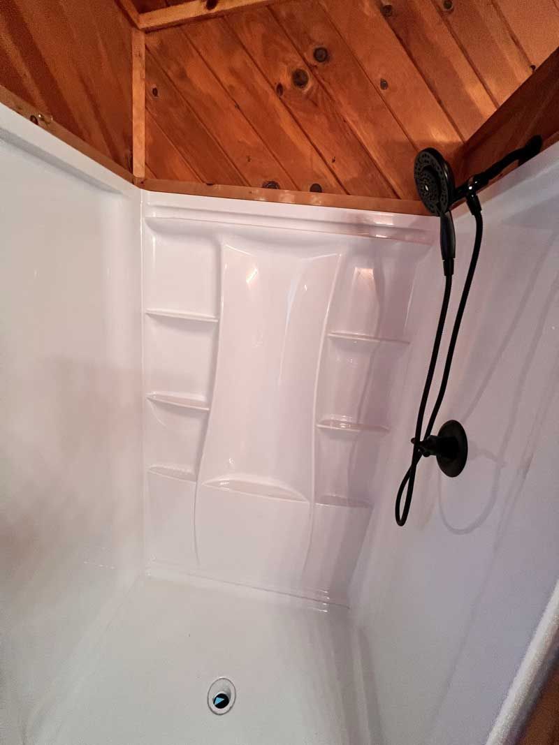 White corner shower stall with built-in shelves, black shower head, wood ceiling.