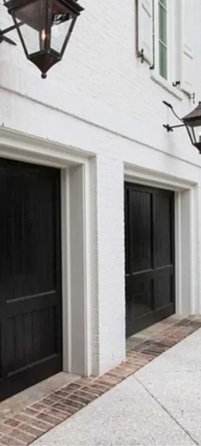 A white house with black garage doors and lanterns on the sidewalk.