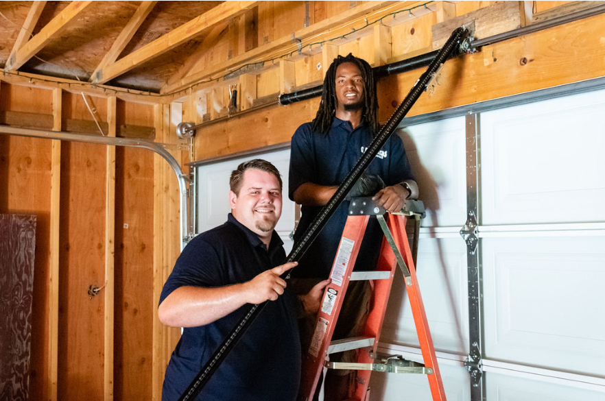 Two men are working on a garage door in a garage.