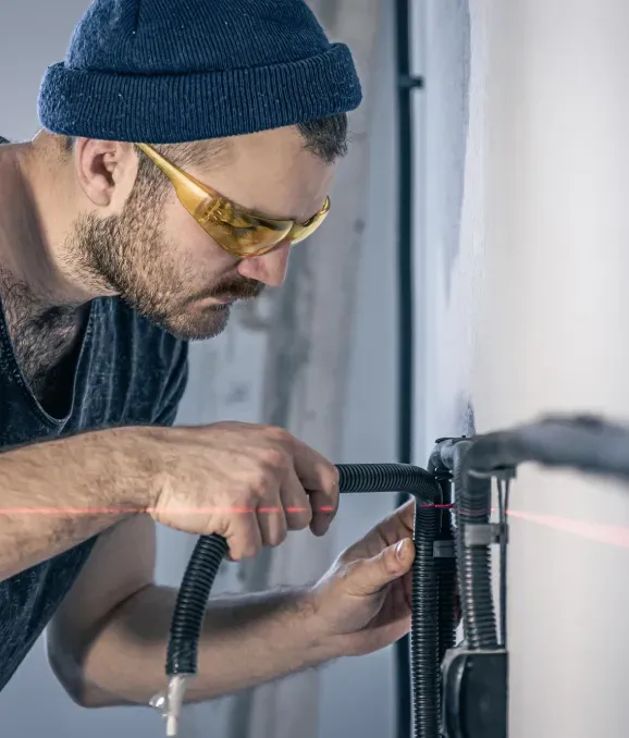 A man wearing safety glasses and a hat is working on a pipe.