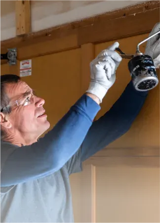 A man wearing safety glasses and gloves is working on a light fixture.