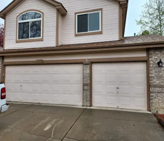 A white truck is parked in front of a house with two garage doors