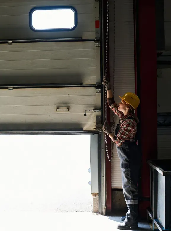 A man in a yellow hard hat is opening a garage door.