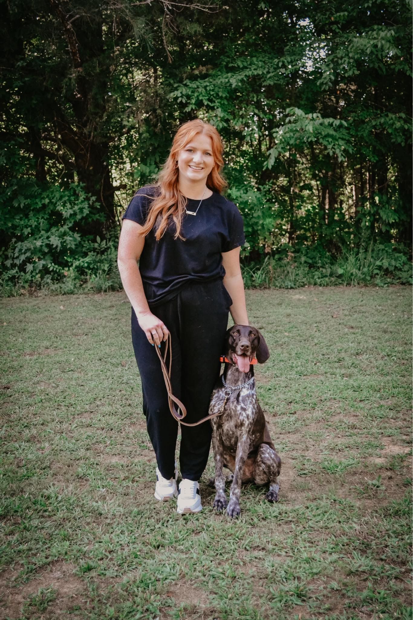 A woman is standing next to a dog on a leash in a field.