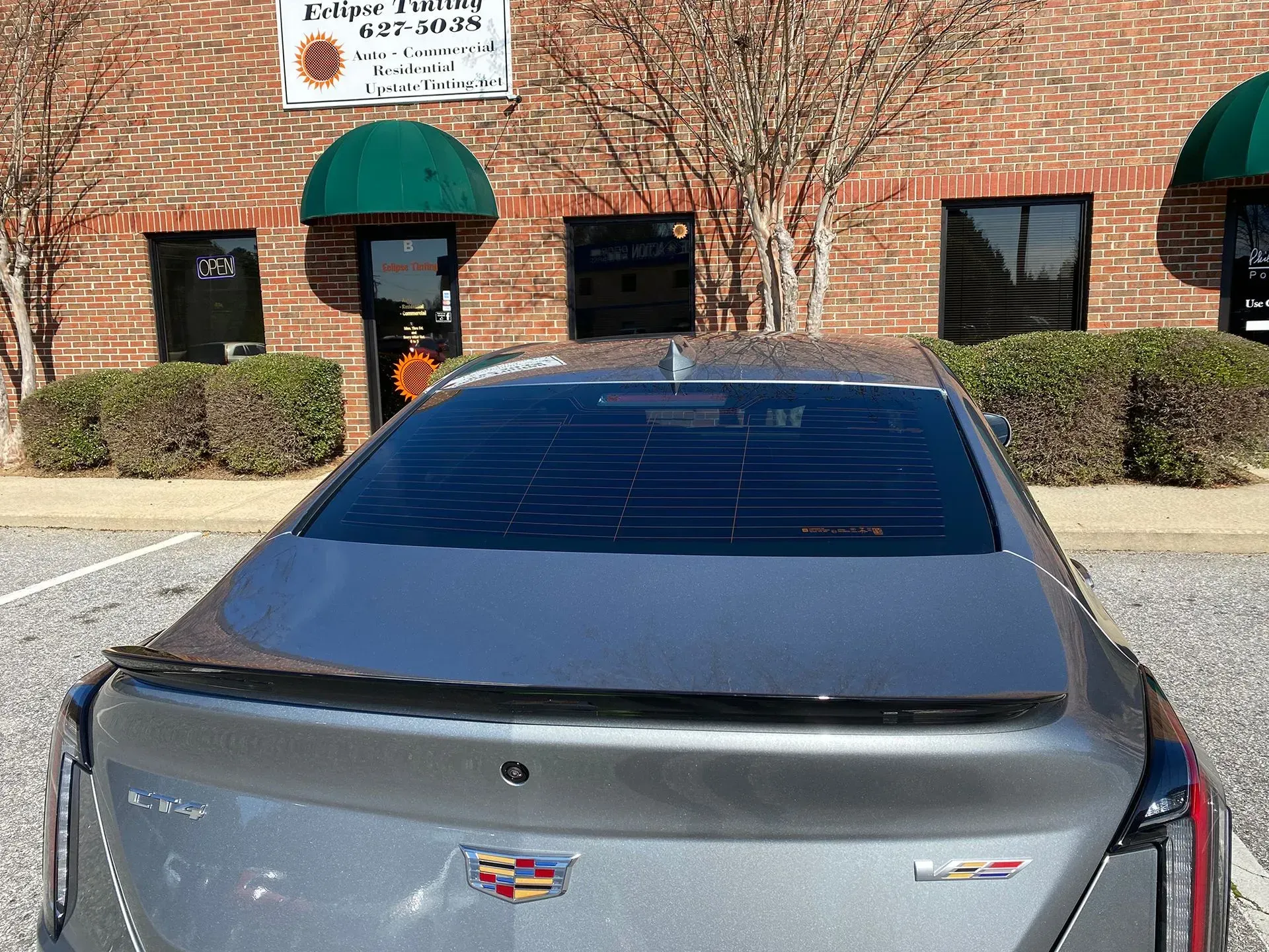 Gray car with tinted windows parked in front of a brick building with green awnings.