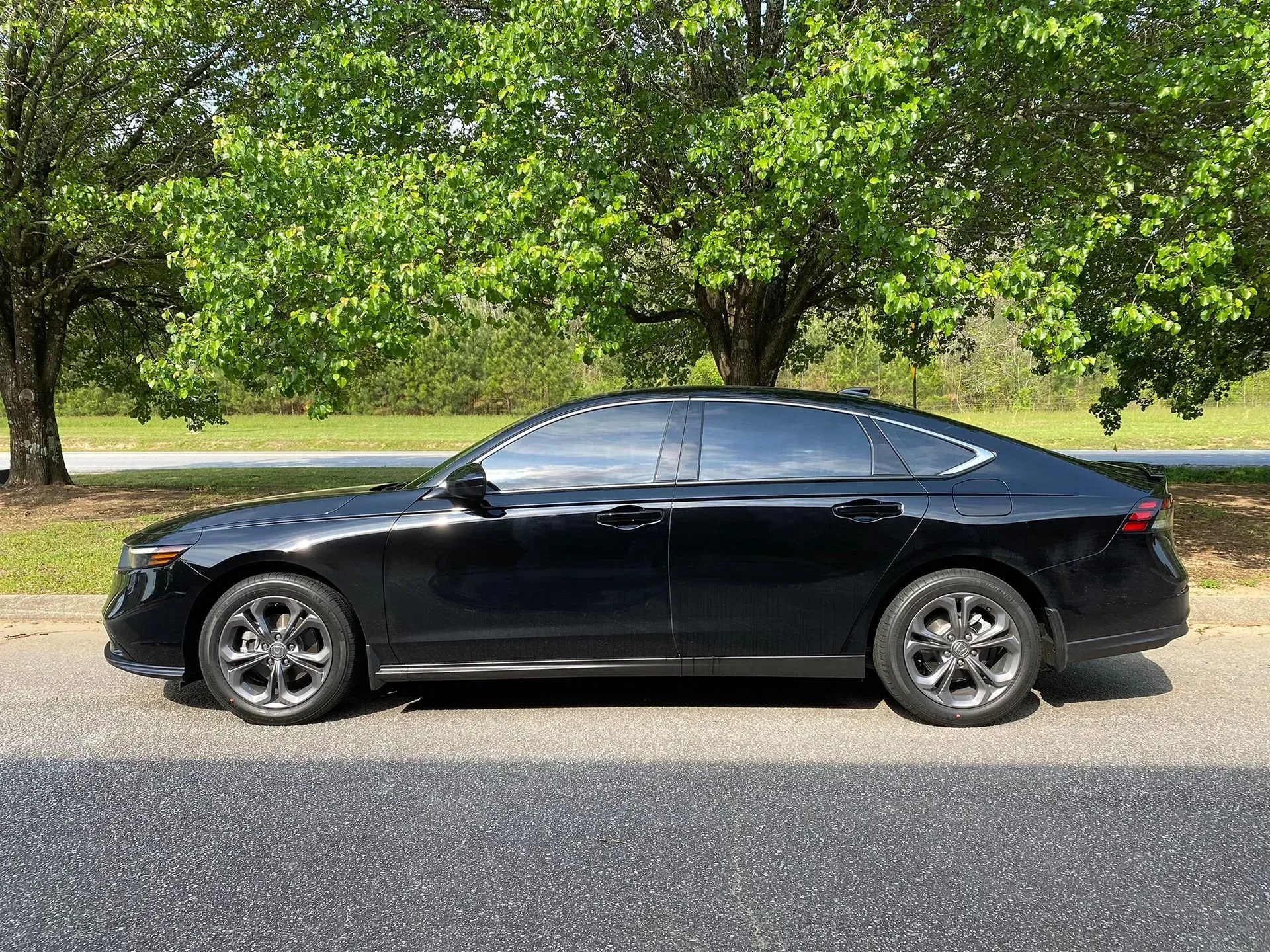 Black sedan parked on a road with trees in the background on a sunny day.