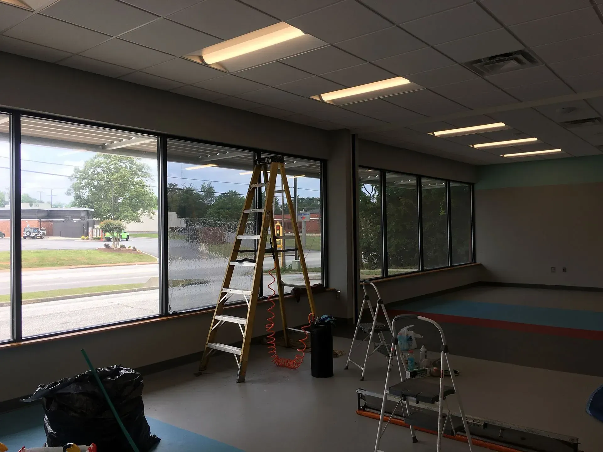 Interior of a room with large windows; a ladder stands near windows; work in progress.