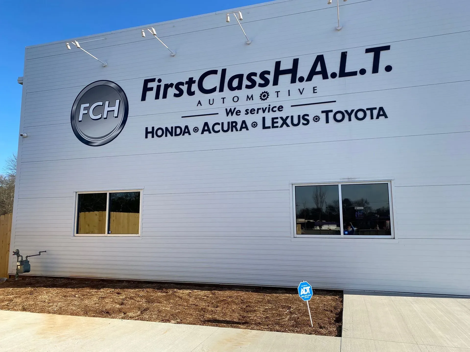 Exterior of First Class H.A.L.T. Automotive building, servicing Honda, Acura, Lexus, and Toyota. White building with large signage.
