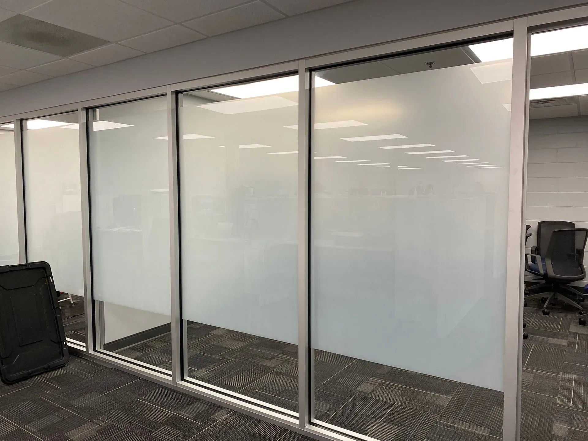 Frosted glass office walls with aluminum frames, carpeted floor, and a black office chair.