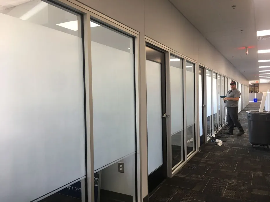 Hallway with frosted glass office walls; a person stands working, holding a tool.