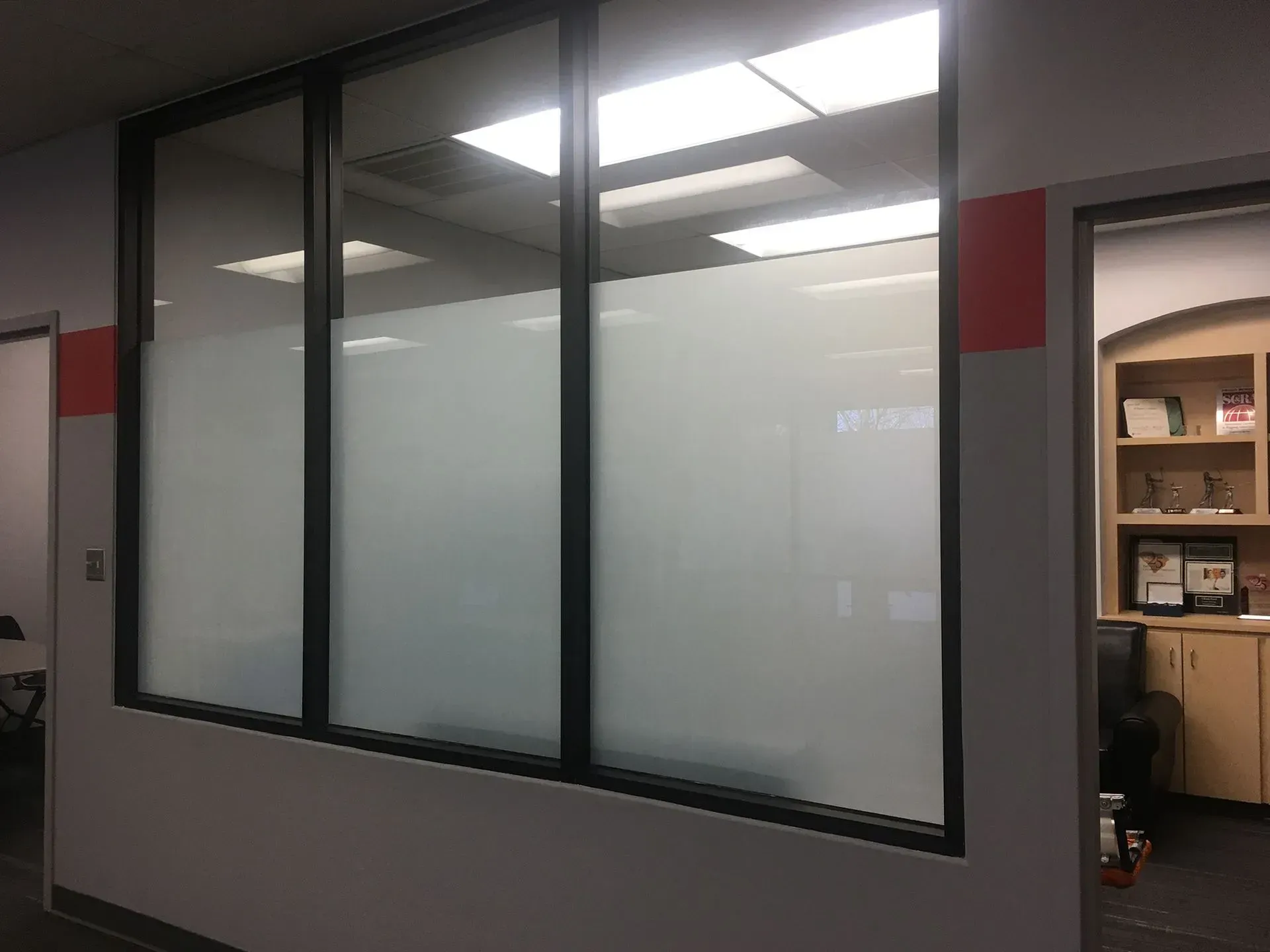 Frosted glass office windows; gray walls with red accents; door to another room on the right.