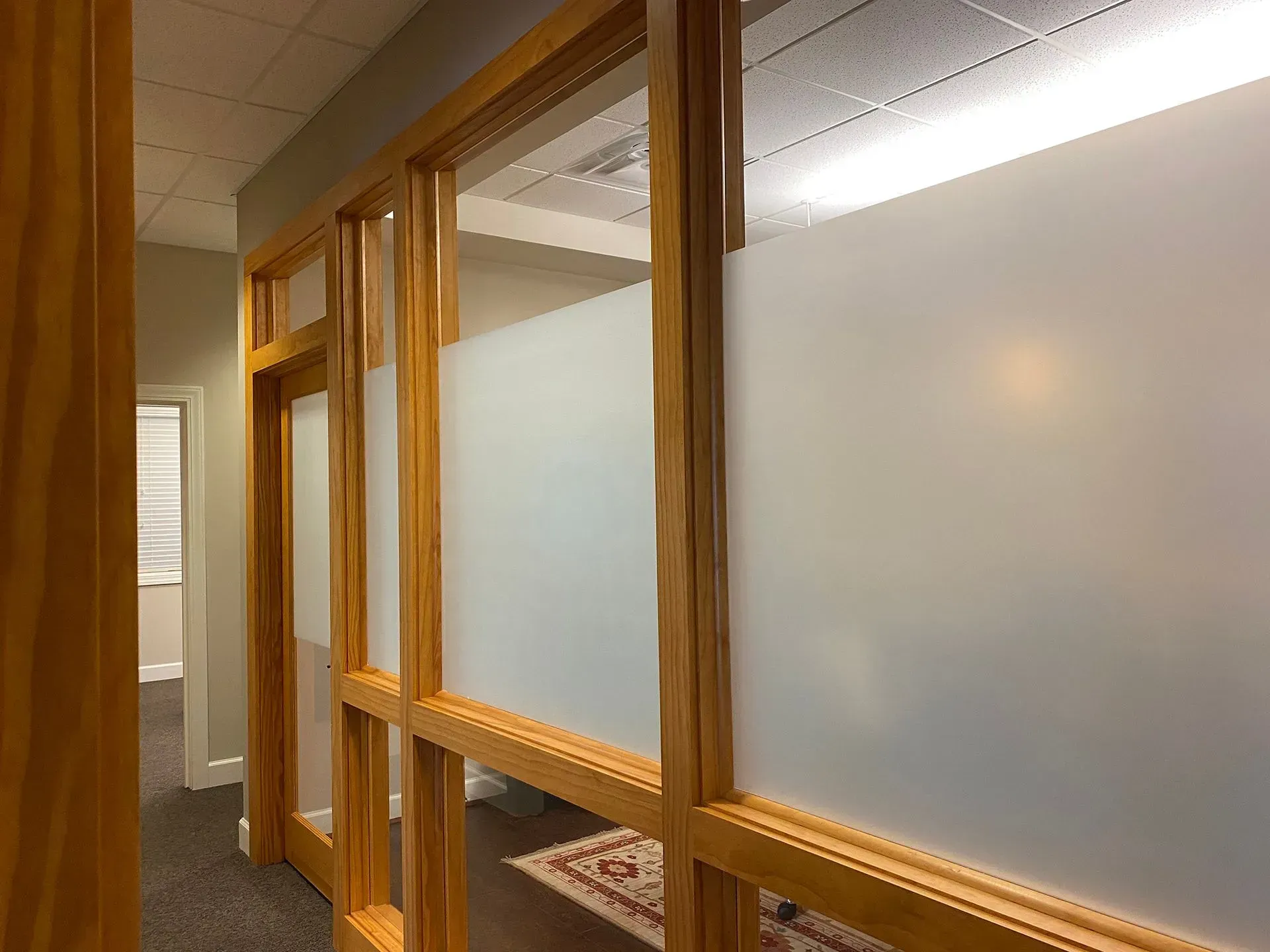 Wooden framed frosted glass office partition with a hallway in the background.