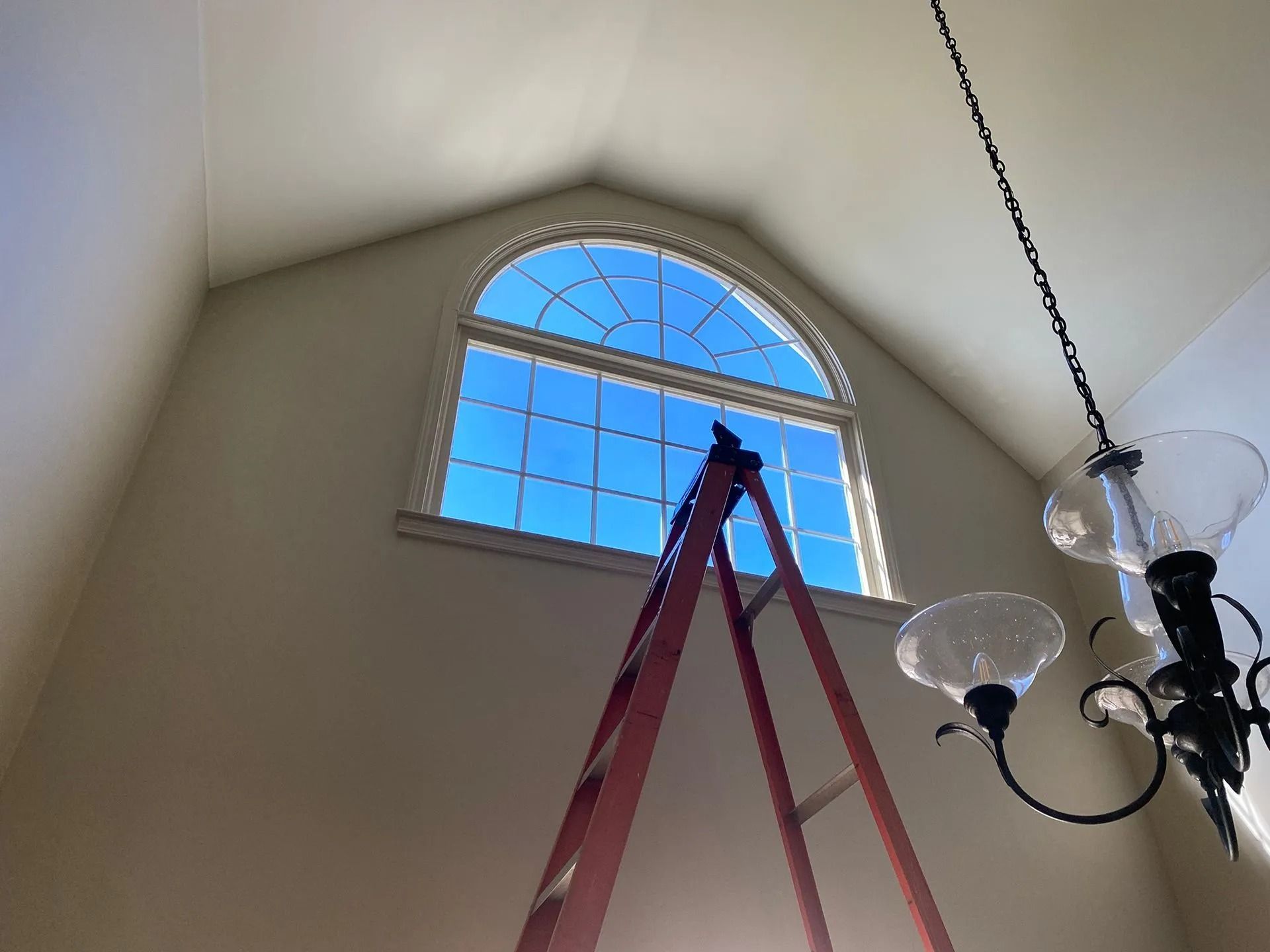 A-frame window with ladder, set against a blue sky. Chandelier hangs in the room.