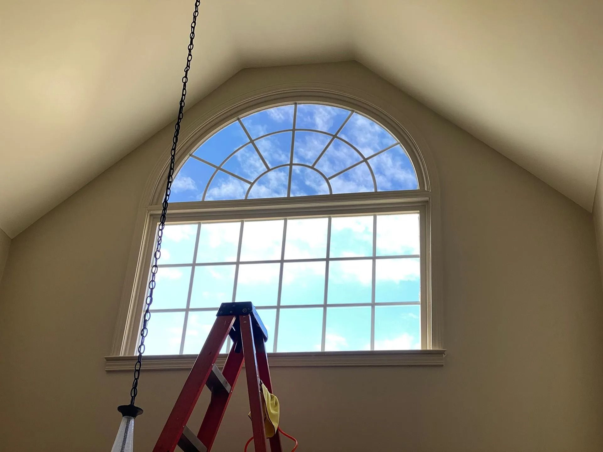 A-frame window with a half-circle top, revealing a blue sky. A red ladder is in front of the window.