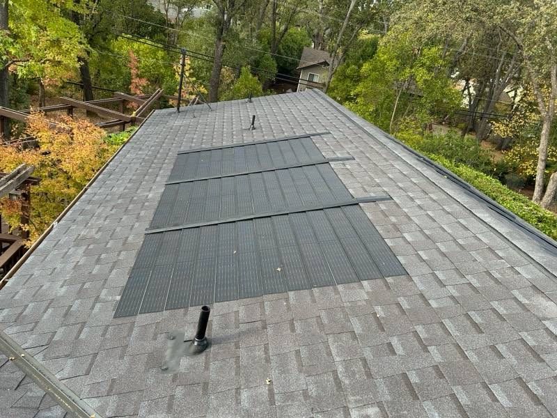 A roof with a solar panel on it and trees in the background.
