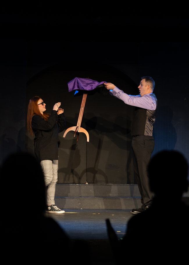 A man and a woman are performing a trick on a stage.