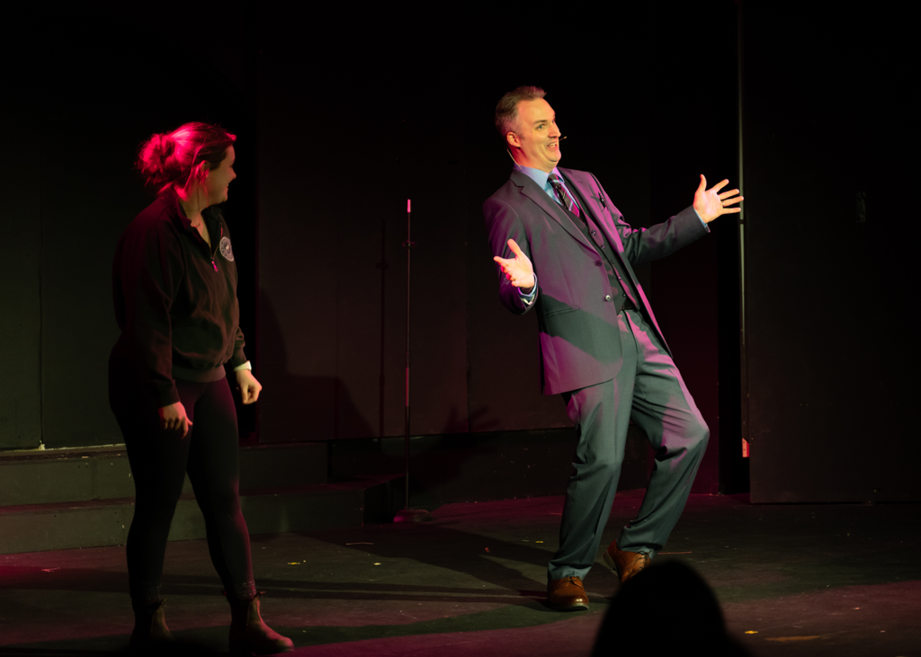 A man in a suit and tie is standing next to a woman on a stage.