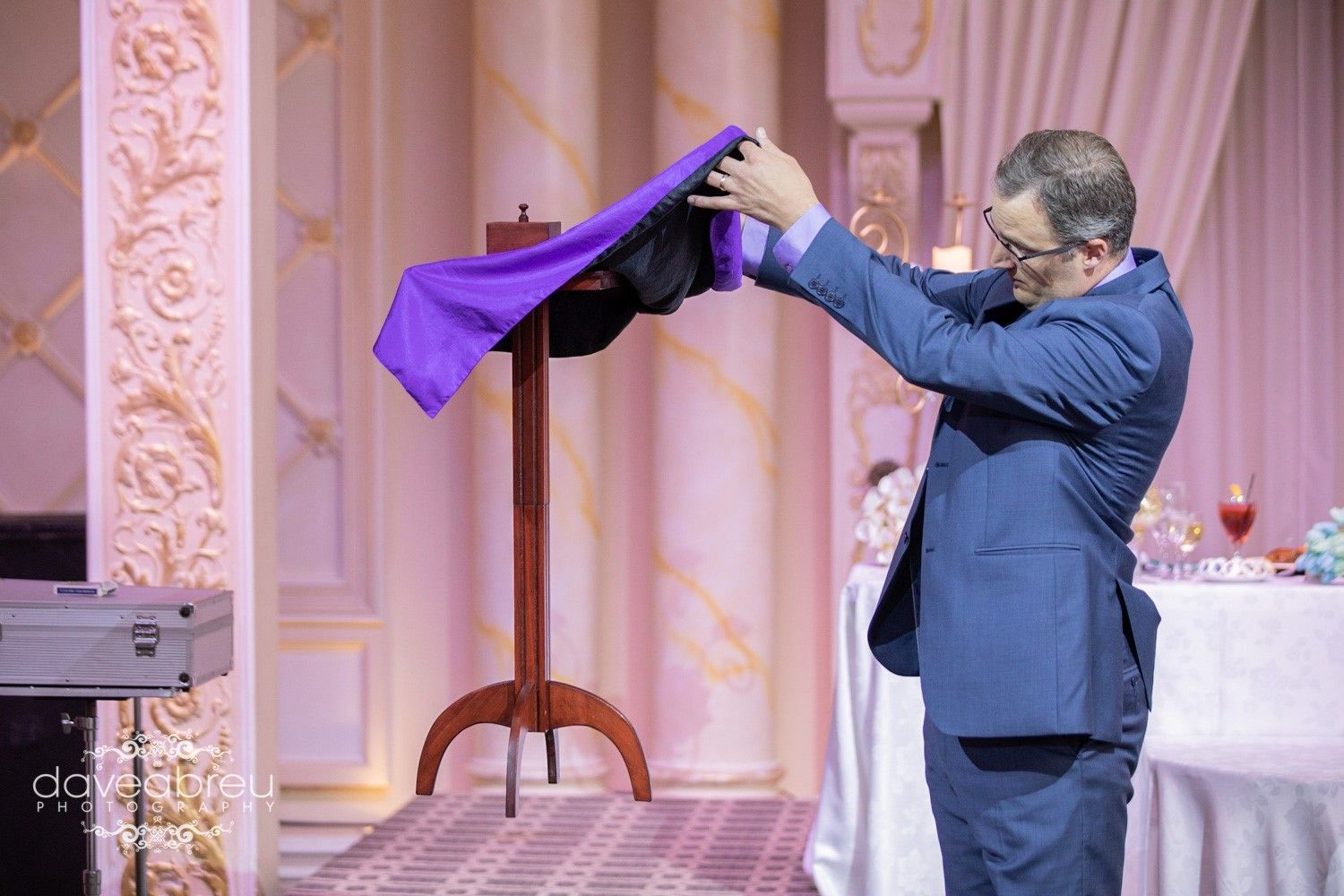 A man in a suit is performing a trick with a purple cloth.