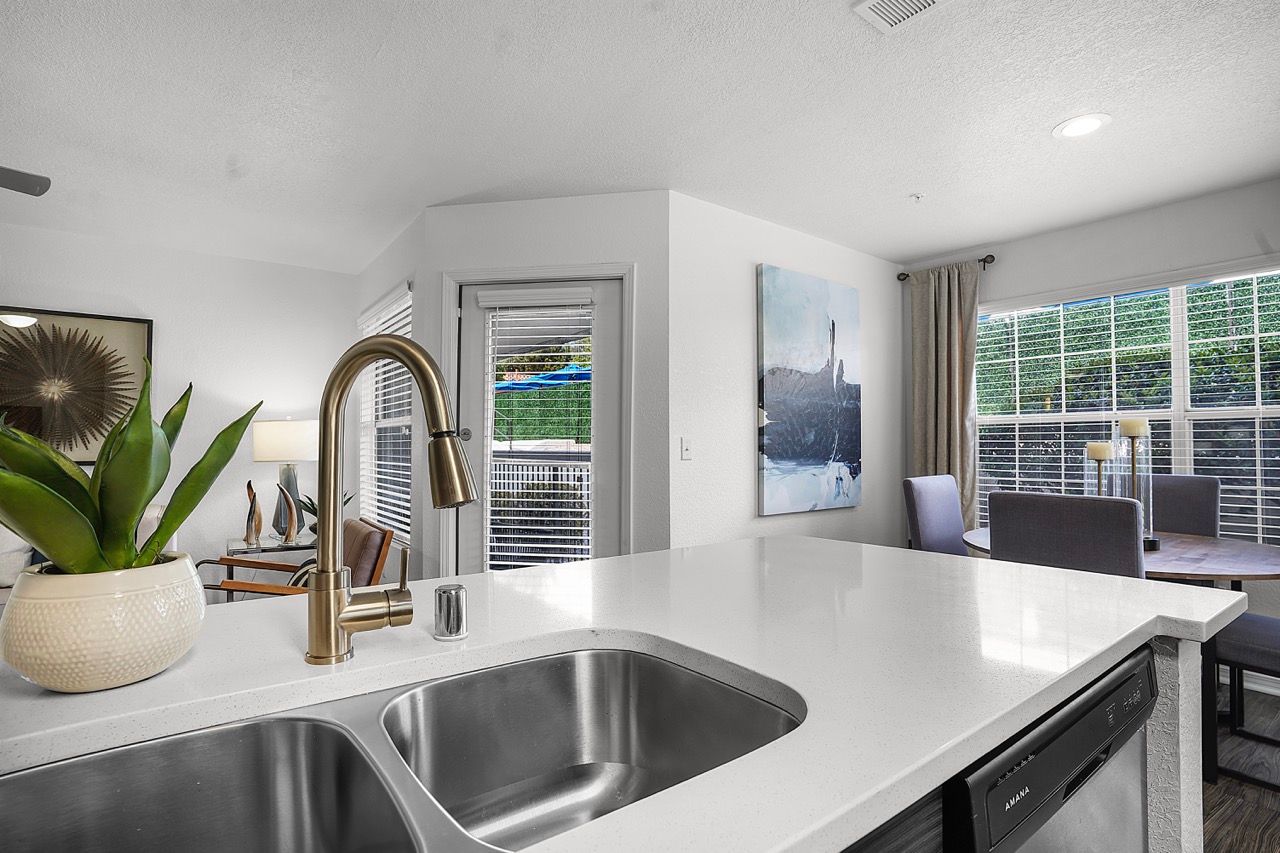 Open-concept kitchen with a white island, double sink, and brass faucet overlooking a bright living area.