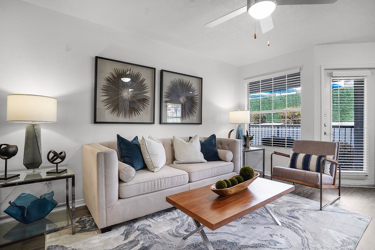 Bright living room with beige sofa, chair, coffee table, and large window blinds.