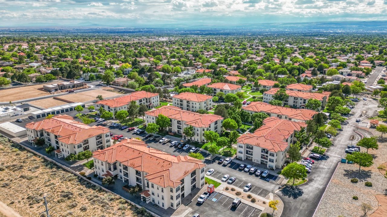 Aerial view of a large apartment community with orange-tiled roofs, green trees, and parking lots.