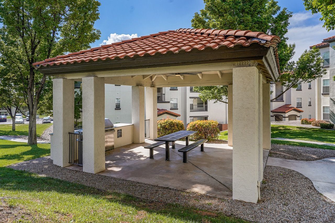 Outdoor pavilion with a grill and picnic table in a landscaped apartment courtyard.
