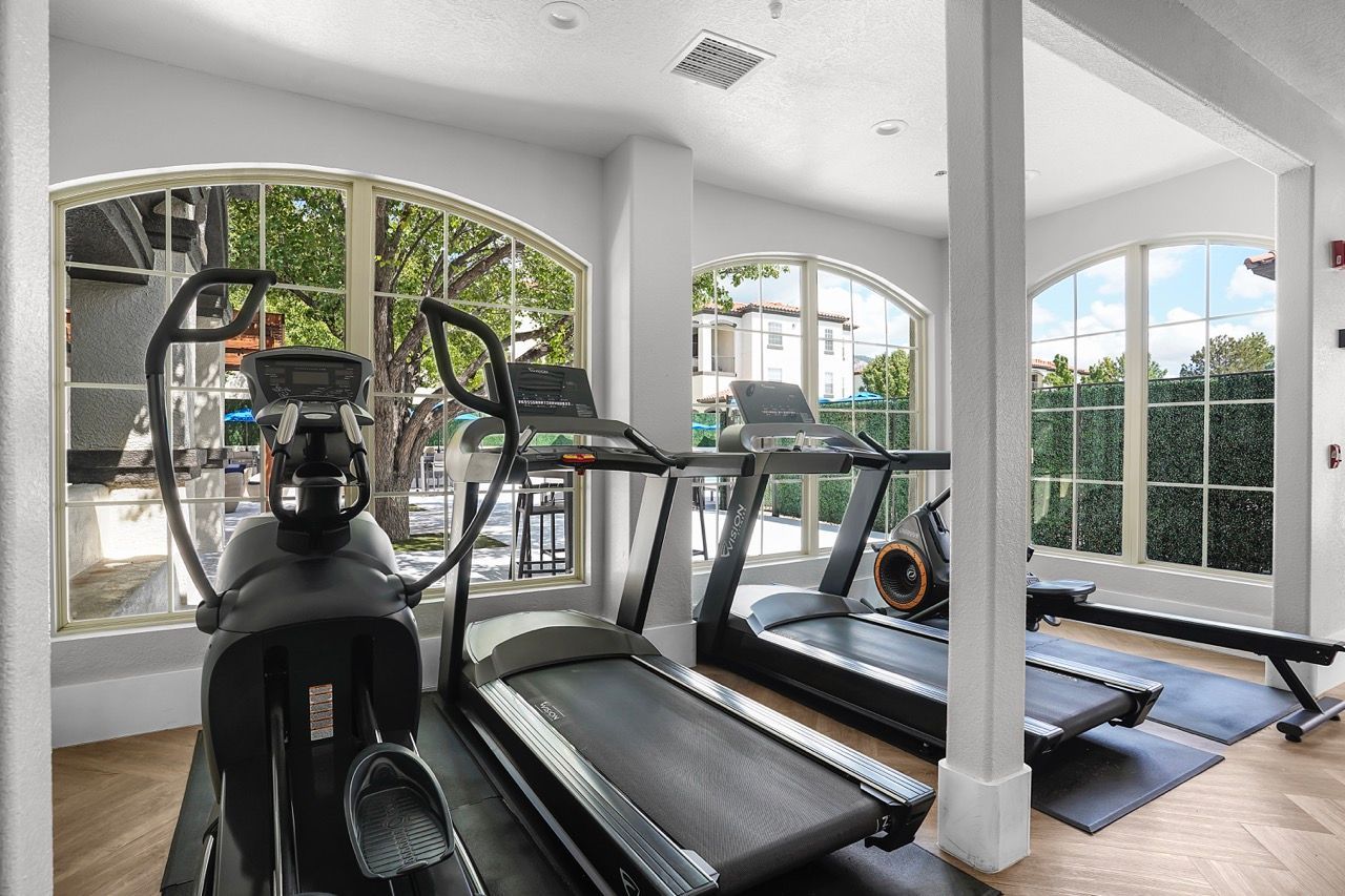Indoor fitness center with treadmills and an elliptical machine by large arched windows.