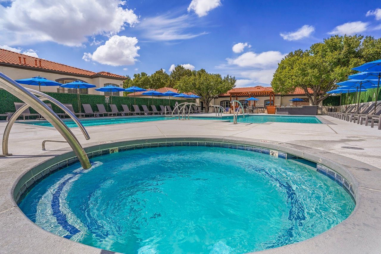 Outdoor community pool and spa area with blue umbrellas and lounge chairs.