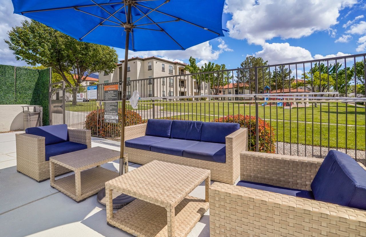 Outdoor community lounge with wicker seating, blue cushions, and a large blue umbrella.