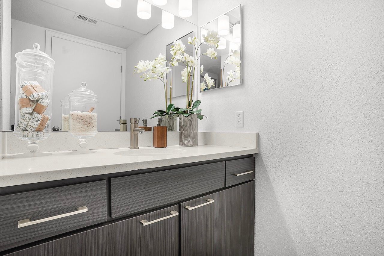 Bathroom vanity with dark wood cabinets, white countertop, mirror, and decorative jars.