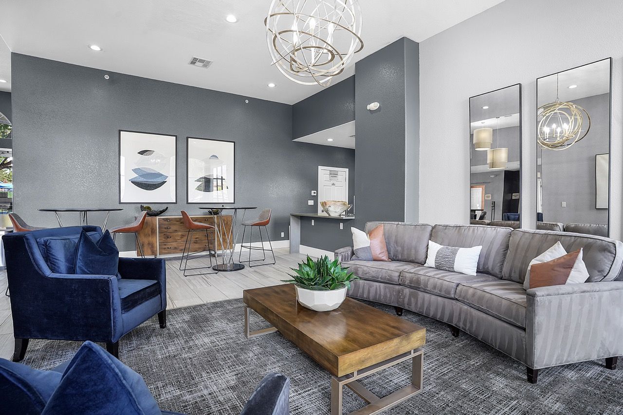 Interior of a modern community lounge with gray walls, a large sectional sofa, and high-top tables.