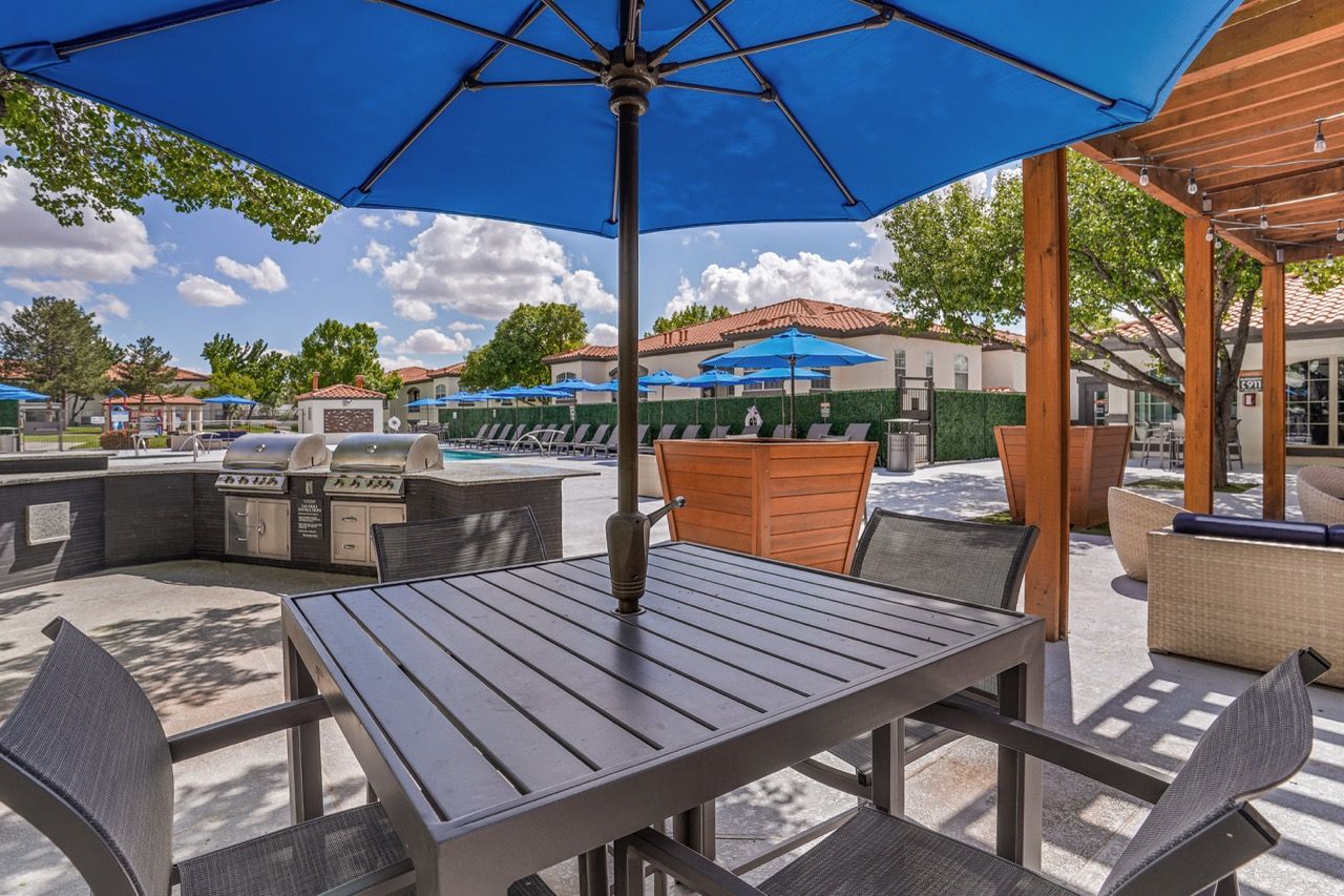 Outdoor community amenity area at an apartment complex with a pool, grills, and blue umbrellas.