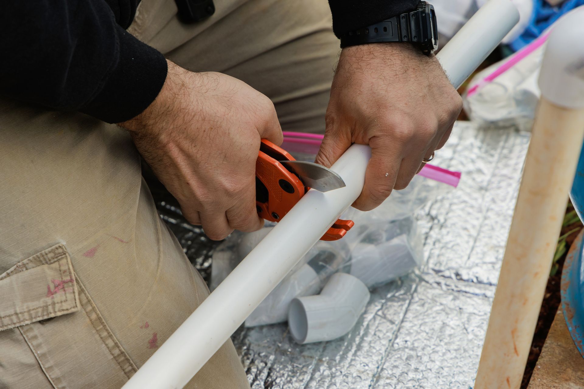 Persona che taglia un tubo bianco in PVC con un tagliatubi, tenendolo con entrambe le mani.