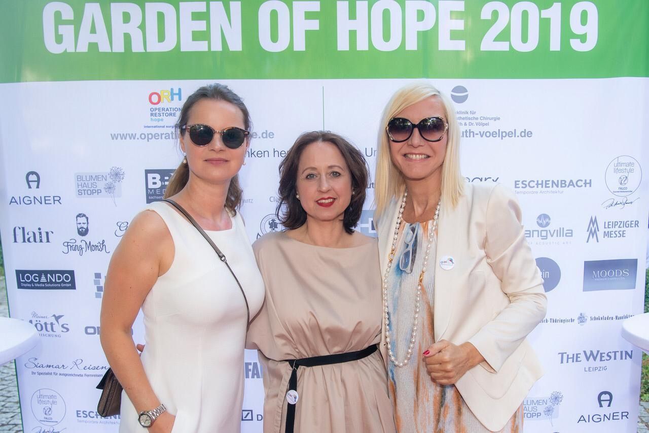 Drei Frauen posieren für ein Foto vor einem Schild mit der Aufschrift „Garden of Hope 2019“