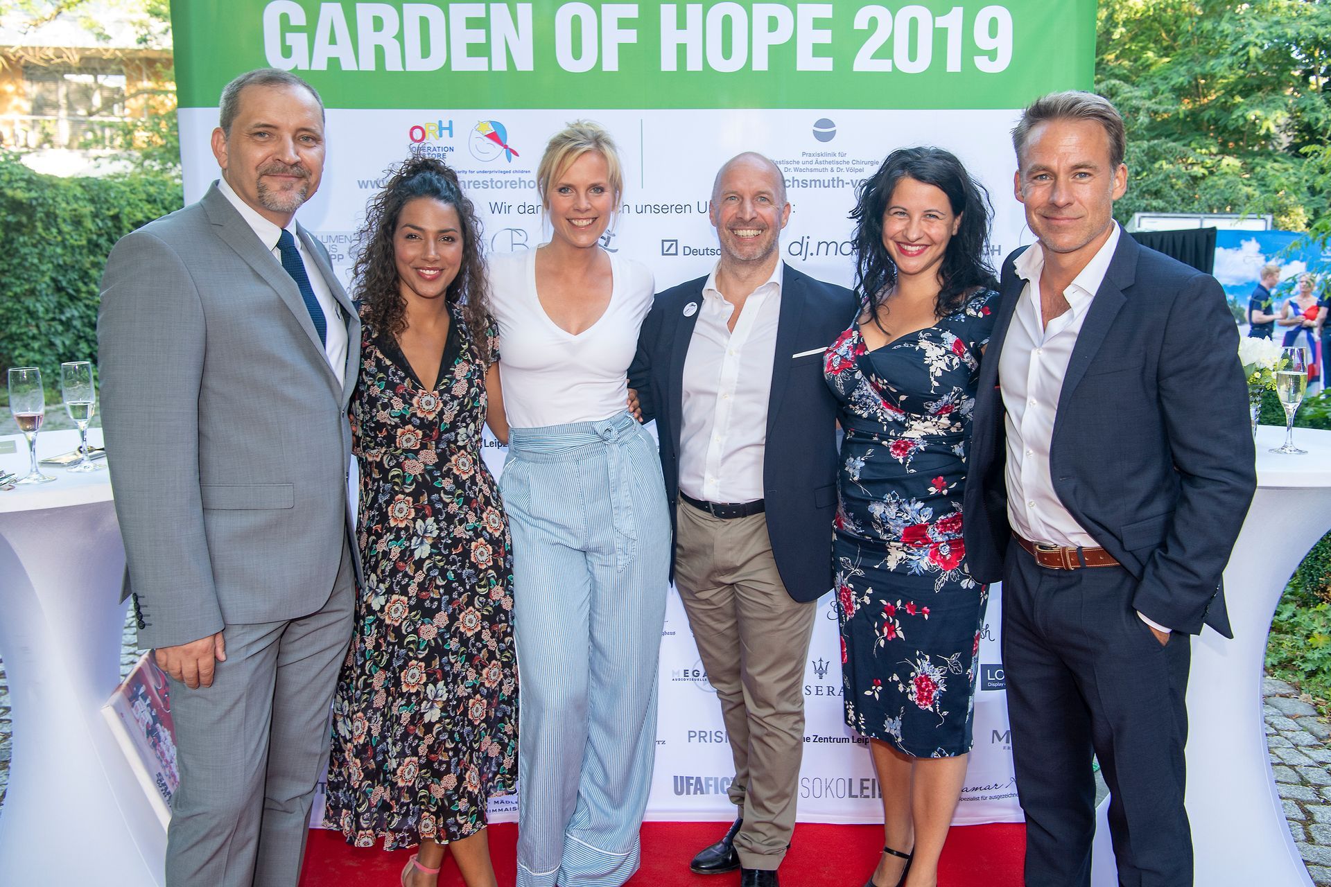 Eine Gruppe von Menschen steht vor einem Schild mit der Aufschrift „Garten der Hoffnung 2019“