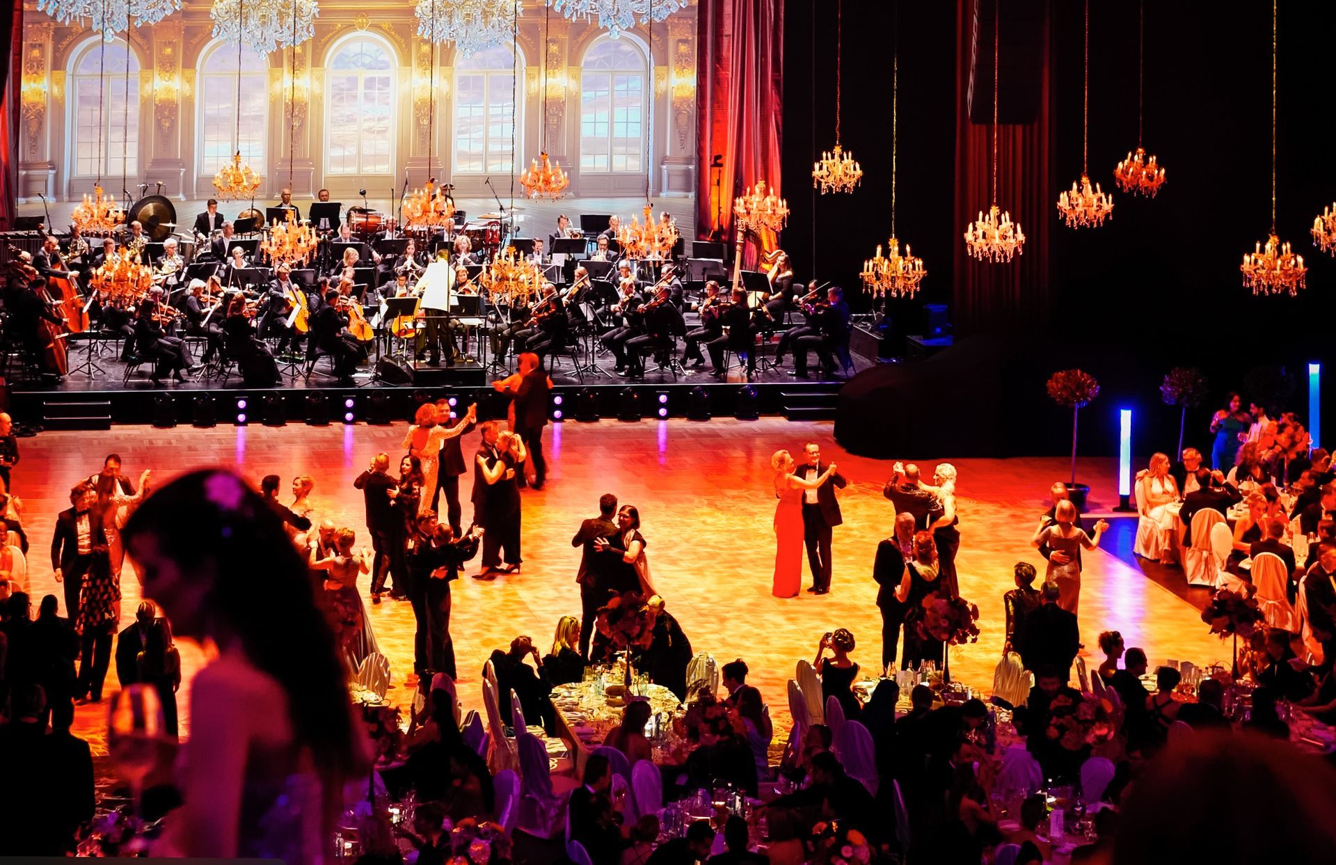 Eine große Gruppe von Menschen tanzt auf einer Bühne mit einem Orchester im Hintergrund