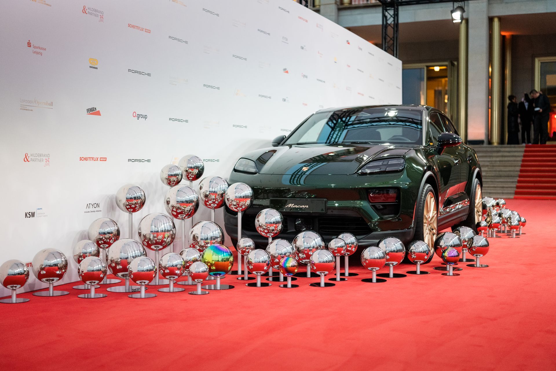 Ein grünes Auto steht auf einem roten Teppich, umgeben von Luftballons