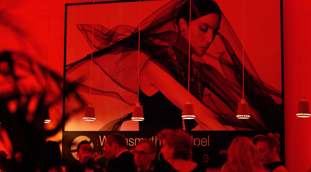 Eine Gruppe von Menschen versammelt sich vor einem Gemälde einer Frau in einem schwarzen Kleid