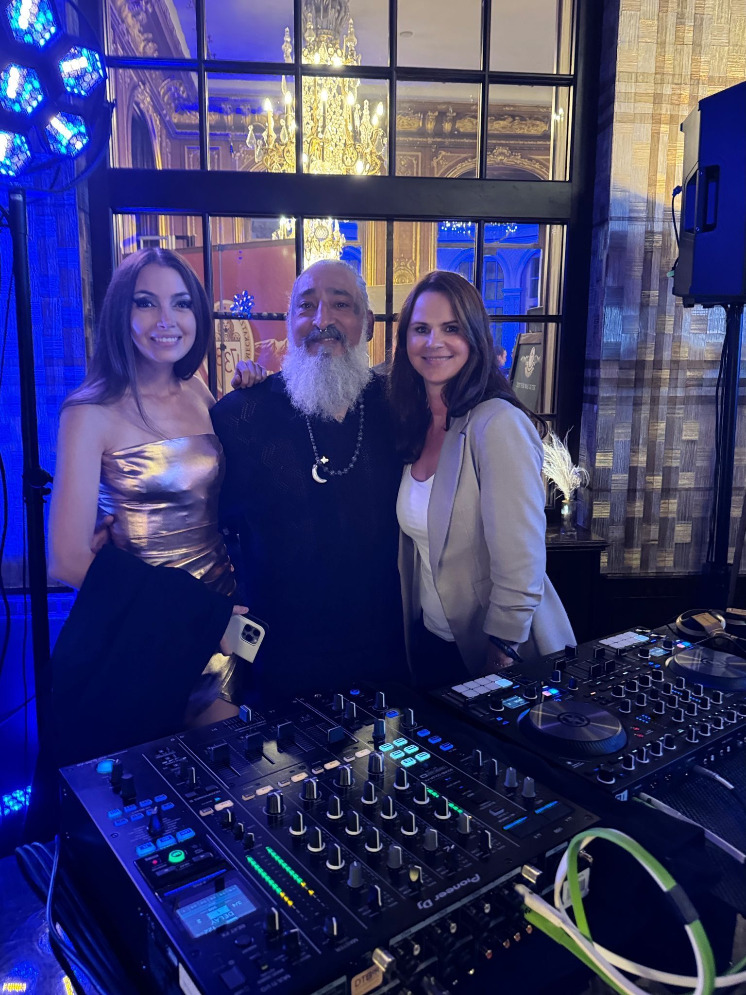 Ein Mann mit Bart und zwei Frauen stehen neben einem DJ-Mixer