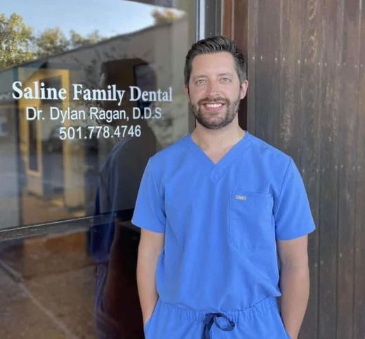 A man in a blue scrub is standing in front of the saline family dental office