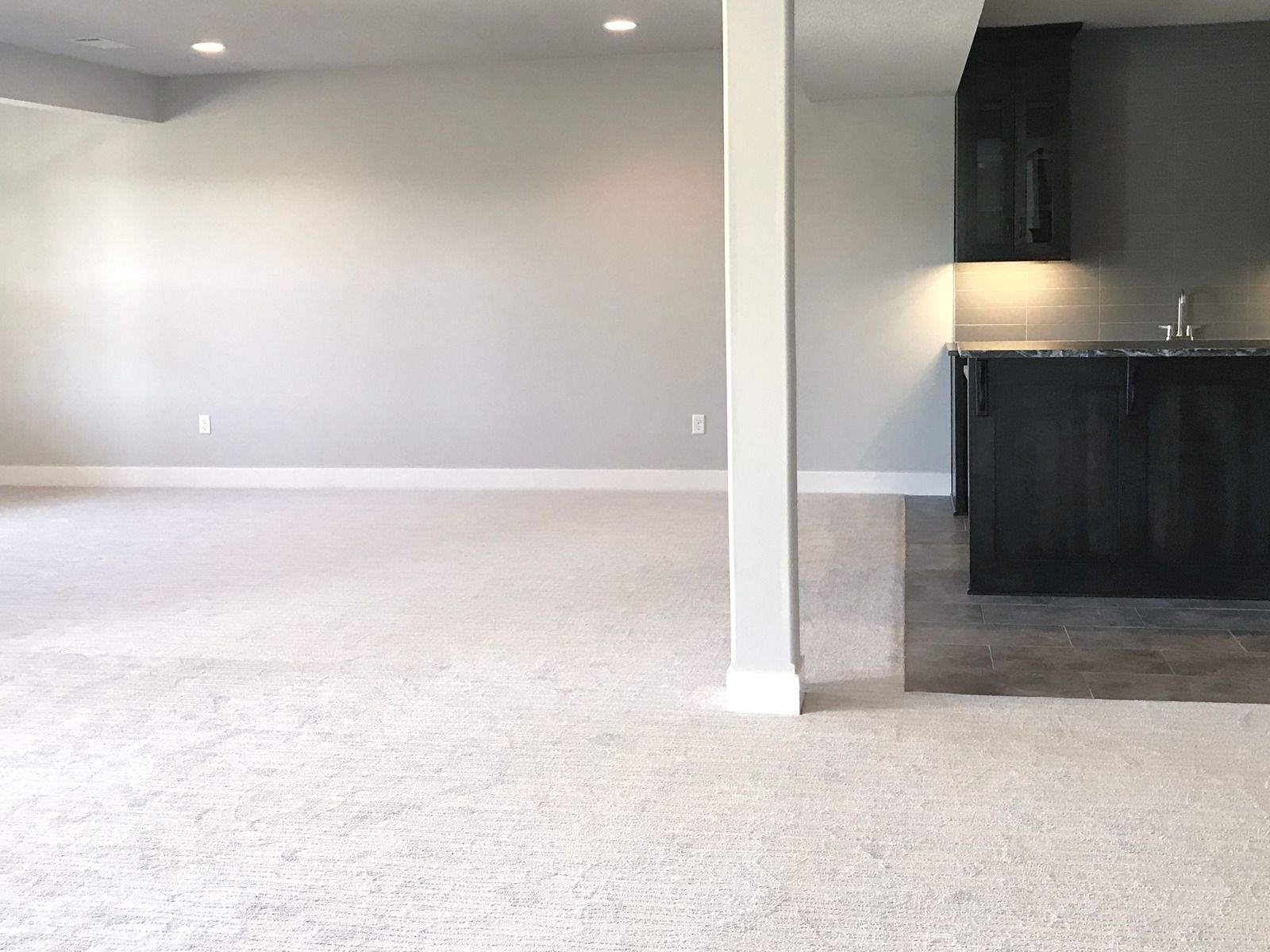An empty room with a white carpet and a kitchen in the background.