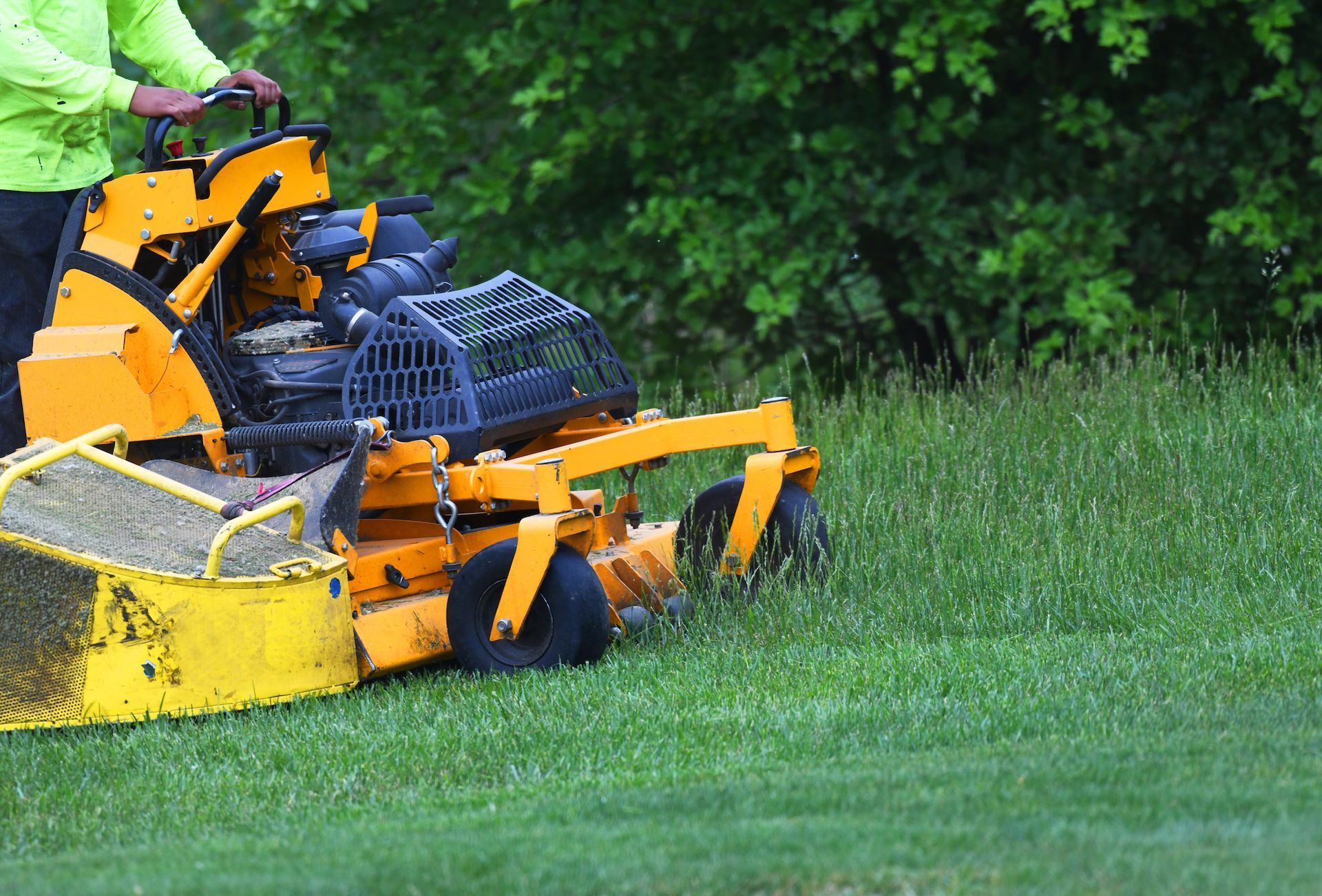 A man is riding a yellow lawn mower on a lush green lawn.
