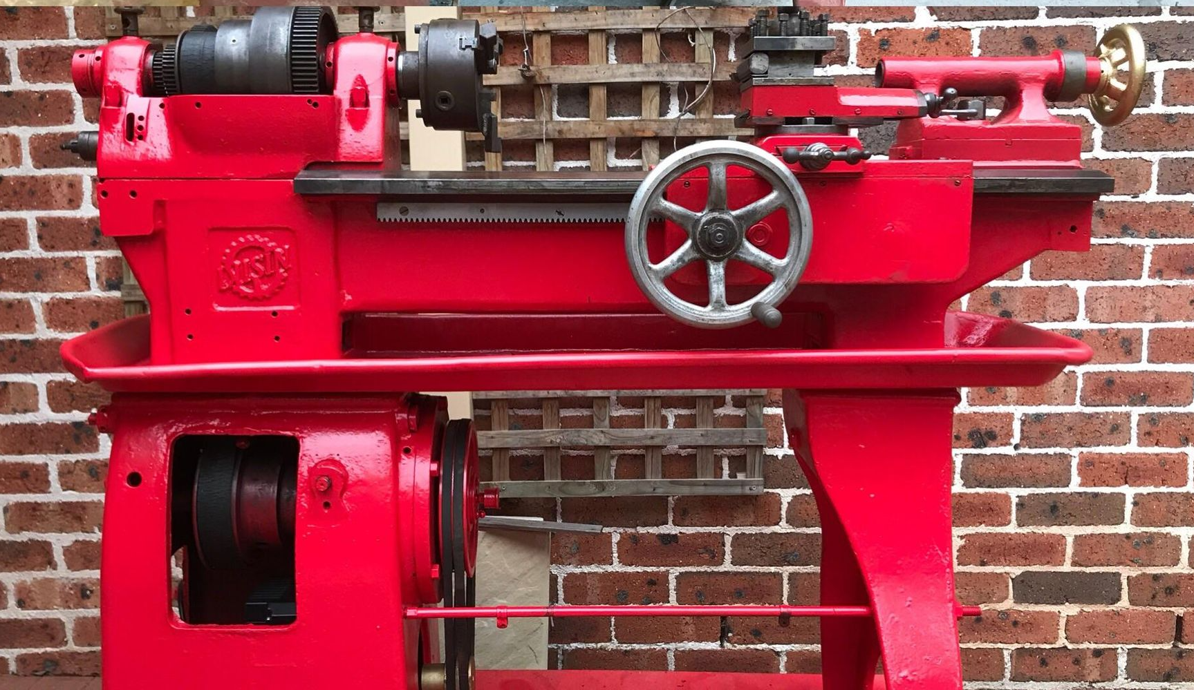Red lathe machine against a brick wall. Metal components, a handwheel, and base.