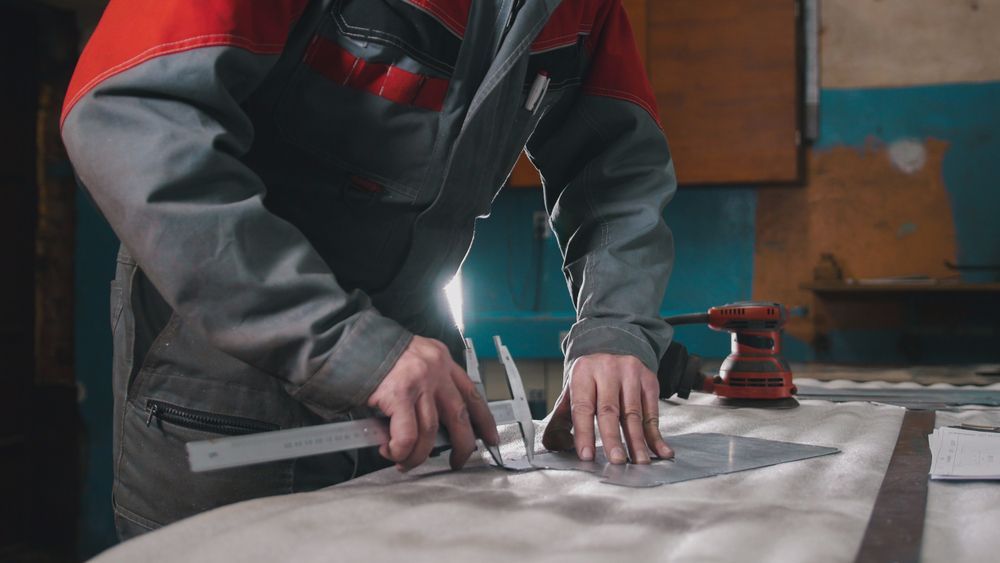 Person in work uniform using calipers to measure metal sheet in workshop.
