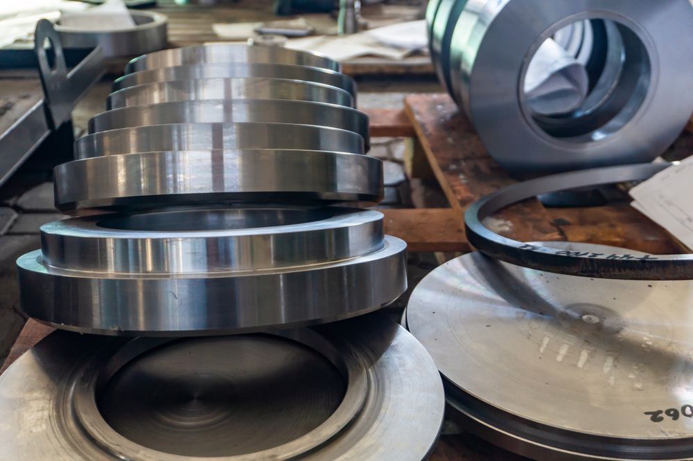 Metal machined discs stacked on a workbench, alongside other metal components.