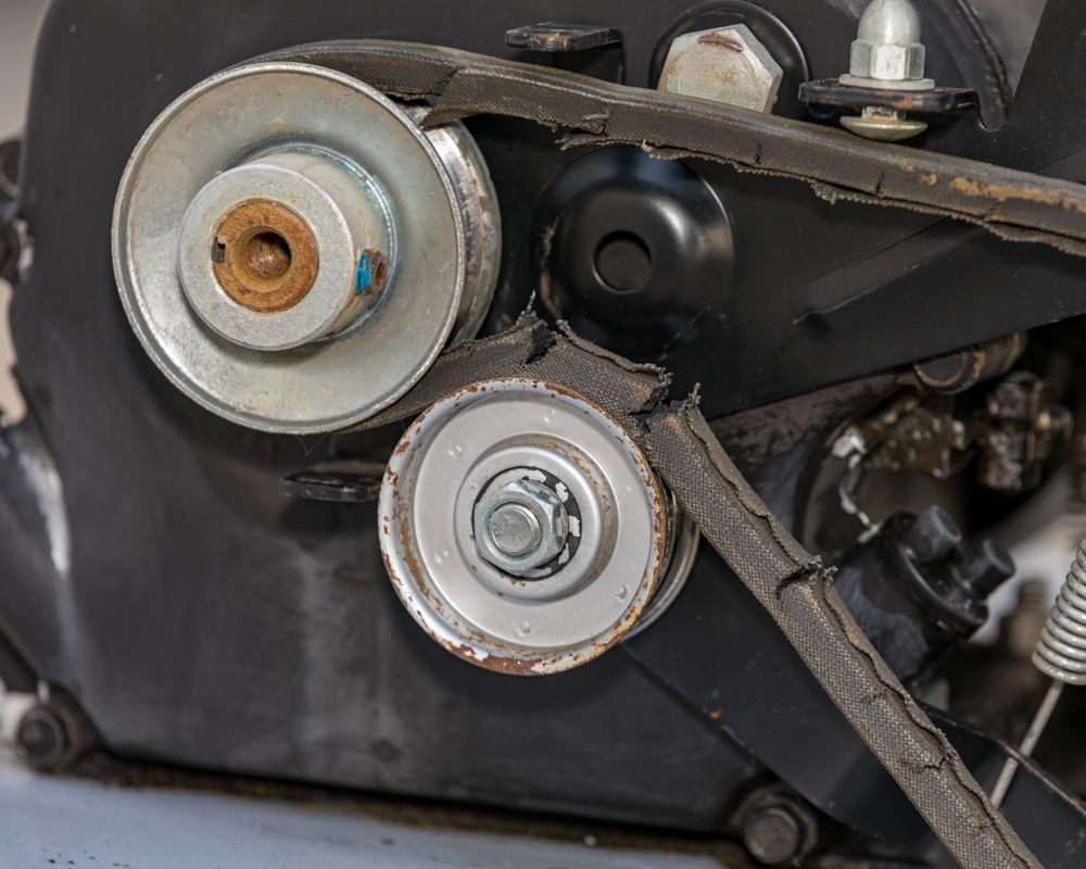 Black engine component with pulleys and a damaged belt.