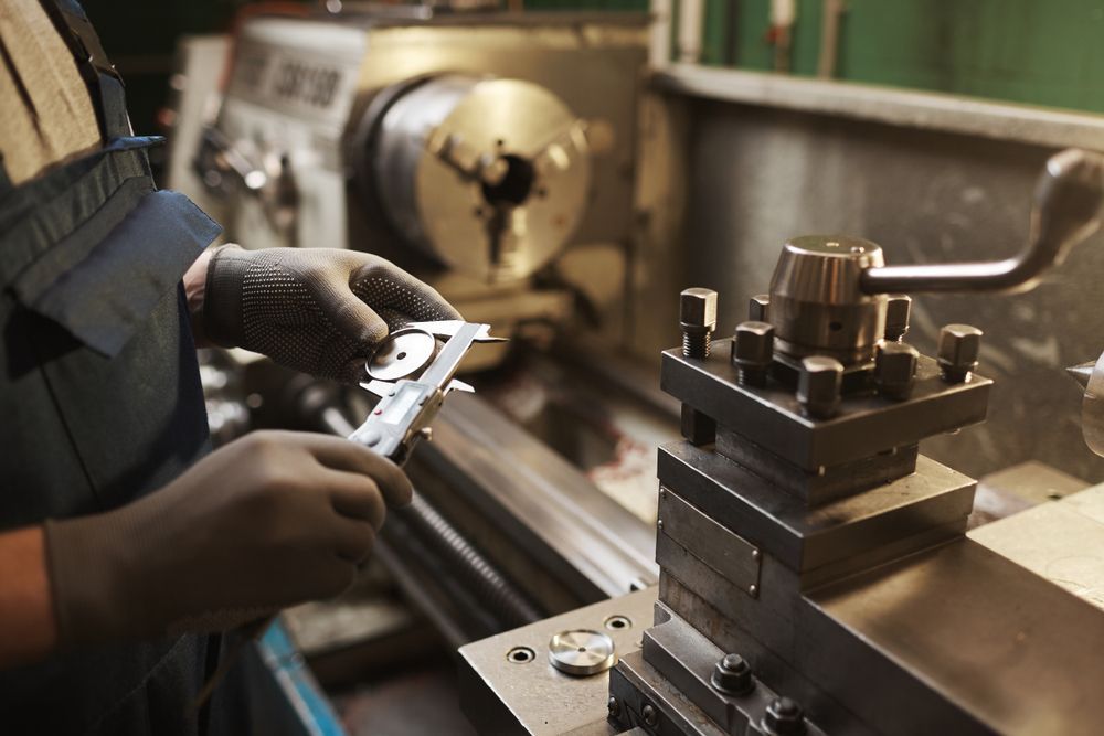 Person using calipers to measure a metal part on a lathe. Workshop setting.