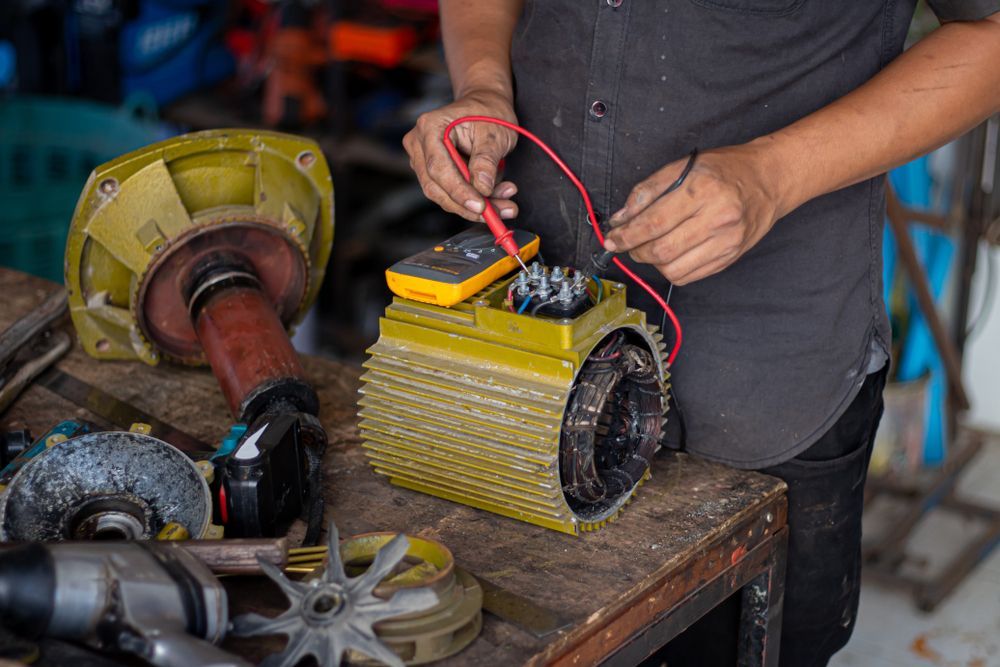 Person using a multimeter on a yellow electric motor, workbench setting.